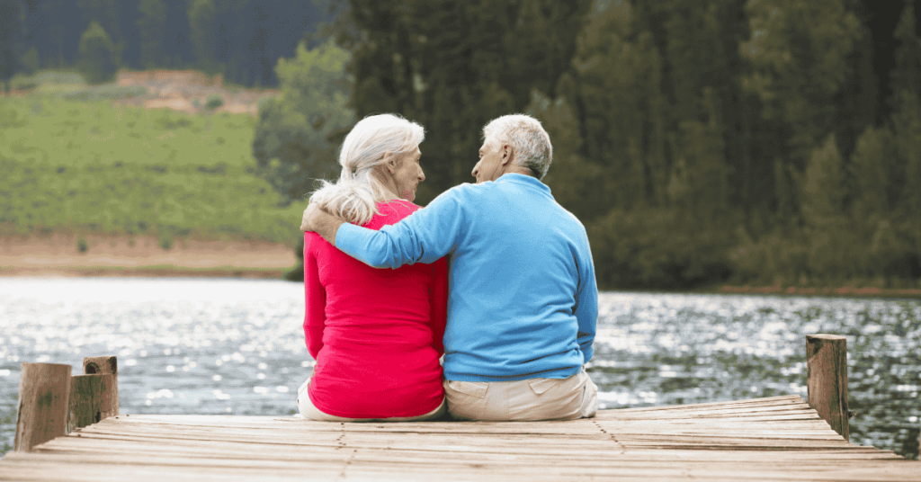 Mature couple wearing sweaters sitting on a dock by a lake discussing acute myeloid leukemia